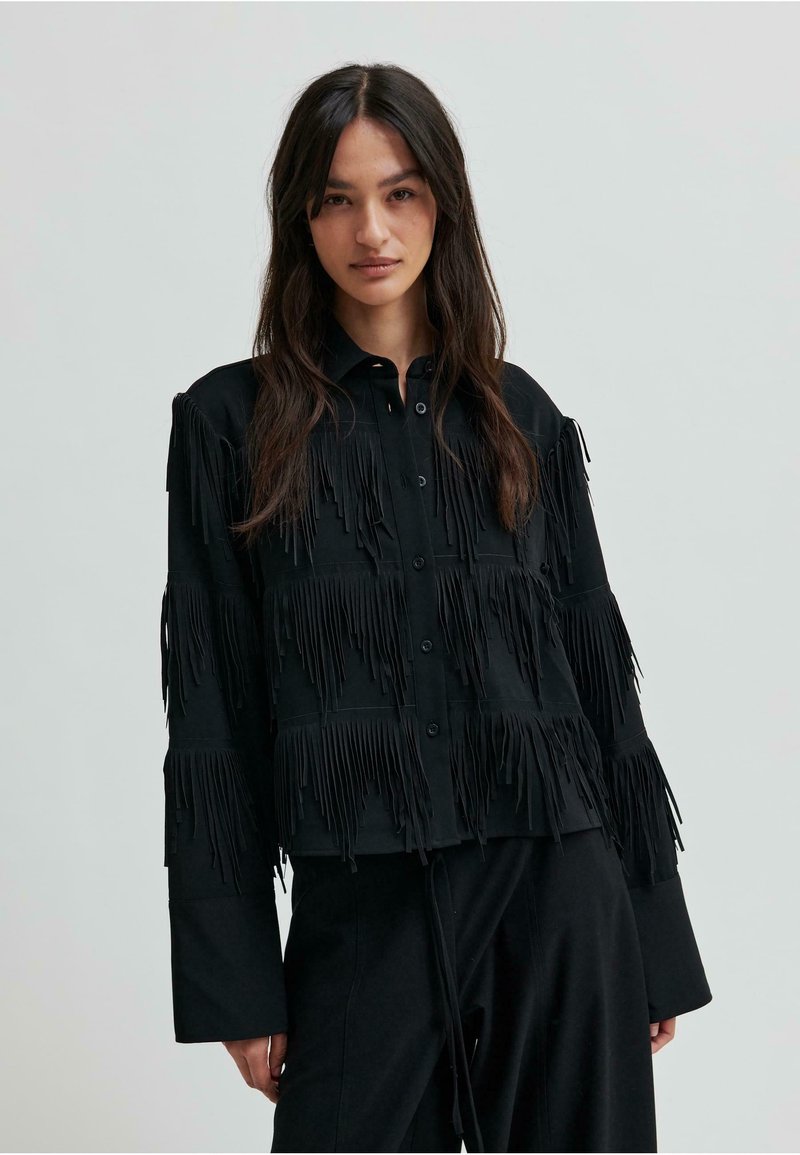Čierna košeľa s gombíkmi so strapcami na prednej strane a na rukávoch. Vyrobená z jemného materiálu s voľným strihom.