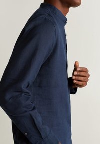 Maglietta a maniche lunghe blu navy realizzata in tessuto testurizzato, con colletto rialzato, dettagli con bottoni e vestibilità morbida.