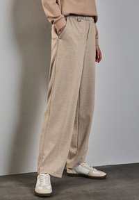Pantaloni beige a gamba larga in un tessuto testurizzato con vita elastica e tasche laterali, abbinati a sneakers bianche.