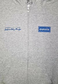 Grå zip-up sweatshirt lavet af blødt stof. Har en frontlomme, blå mærke tekst "oasis" og håndskrevet tekst "Definitely Maybe."