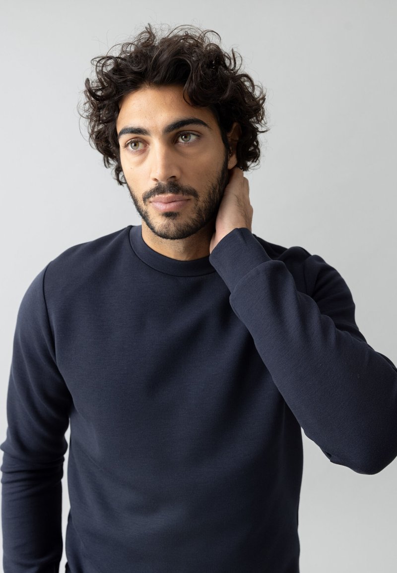 Sudadera de color azul marino hecha de tela texturizada, con cuello redondo y mangas largas, llevada por un hombre con cabello rizado.