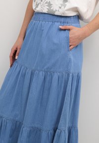 Ljusblå denimmaxi-klänning med ett lagerdesign, elastisk midja och sidoficka. Mjuk textur och avslappnad passform.