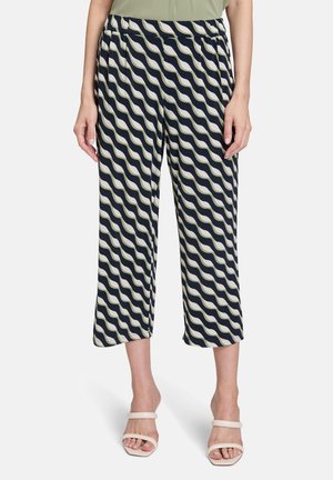 Marineblauwe broeken met een golvend crèmekleurig patroon, elastische tailleband, cropped lengte, lichtgewicht stof, gecombineerd met minimalistische witte sandalen.