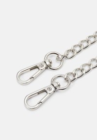 Chaînes en métal argenté, chacune terminée par un fermoir à homard à ressort, reliées par des anneaux ronds sur fond blanc.