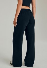 Sorte sweatpants med en afslappet pasform, elastisk talje og sidesømme. Stoffet ser blødt og let tekstureret ud.