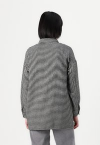 Black and white checked oversized shirt with a collared neck and long sleeves, made from textured fabric, featuring buttoned cuffs.
