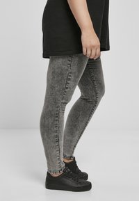 Szürke farmer leggings diszkrét kopott textúrával, formázott dizájnnal és bokáig érő hosszal, fekete sportcipővel párosítva.