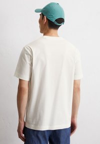 Crème-kleurig katoenen t-shirt met korte mouwen, rechte snit en een gladde textuur, gecombineerd met een cèpe kleur baseballcap.
