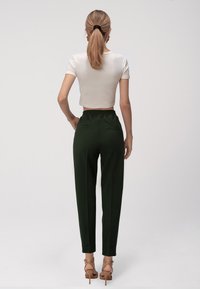 Pantaloni verdi a gamba stretta con vita arricciata, abbinati a una camicia bianca corta. Viene indossato un paio di tacchi con cinturini alla caviglia.