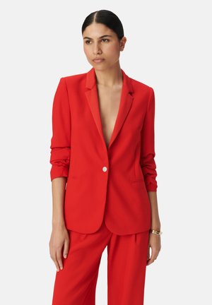 Rode blazer met een geknipt kraag en een enkele zilveren knop. Getailleerde pasvorm, opgerolde mouwen, gecombineerd met bijpassende rode broek. Soepele stof.