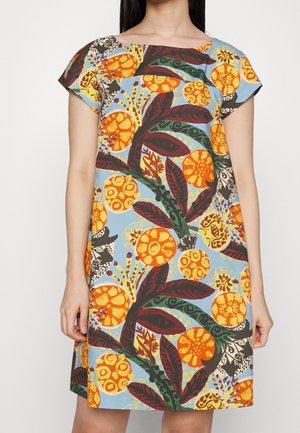 Femme portant une robe à manches courtes avec des motifs floraux orange vif et des feuilles vert foncé sur un fond bleu clair.