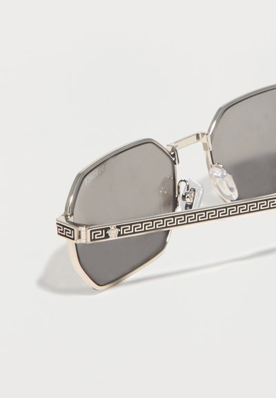 Εξαγωνικά γυαλιά ηλίου με σκοτεινούς φακούς και χρυσοχάλκινα τμήματα στα πλαϊνά, με μοτίβο κλειδί της Ελλάδας και έμβλημα κεφαλής Μέδουσας.