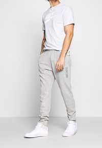 Ljusgrå Nike-t-shirt med en logotyp på framsidan, ihop med ljusgrå joggers med texten "JUST DO IT". Vita sneakers med en jämn yta.