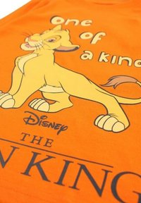 T-shirt en coton orange avec un graphisme d'un lion jaune, accompagné du texte « Unique en son genre » au-dessus et « Disney Le Roi Lion » en dessous en lettres noires.