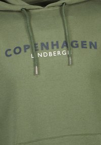 Sudadera verde oliva con un estampado frontal que dice "COPENHAGUE LINDENBERG." Incluye cordones con puntas de plata y una tela texturizada.