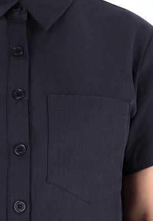Camicia a maniche corte di colore blu navy scuro con chiusura a bottoni, dotata di una piccola tasca sul petto e una texture in tessuto liscia e leggera.