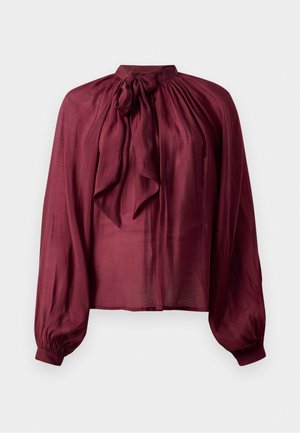 Burgundy long-sleeve blouse with high neck and tied bow, loose fit, and gathered cuffs, displayed on a white background.