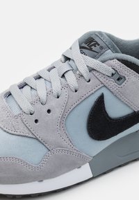 Zapatillas de ante y textil en gris con un Swoosh negro, cordones grises y una suela texturizada. Presenta acentos cosidos y un collar acolchado en gris.