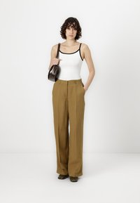 Pantalones de pierna ancha color caqui con una textura suave, cintura alta y bolsillos delanteros; combinados con un top sin mangas blanco y un bolso oscuro.