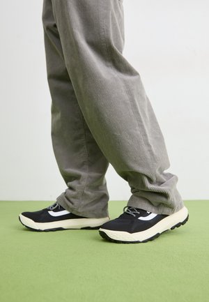 Sorte joggesko med hvite detaljer, med en teksturert overdel, tykk såle og svarte lisser; kombineres med grå cordbukser.