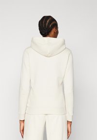 Krämfärgad hoodie i mjukt material, med en stor huva, åtsittande ärmslut och en något avsmalnande design vid midjan.