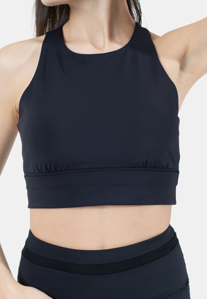 Musta urheilullinen crop-top, jossa on korkea kaula-aukko, ribbid-textuuri ja kerrotut sivut. Omistaa joustavan kankaan, joka sallii liikkumisen.