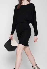 Czarna sukienka z długim rękawem o dopasowanym kroju, w połączeniu z czarną i kremową torebką, noszona z wzorzystymi botkami za kostkę.