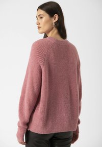 Pulover roz texturat, cu o croială lejeră și mâneci raglan. Are guler și manșete cu model canelat, asortat cu pantaloni negri.