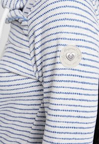 Sudadera a rayas de algodón en blanco y azul, con un parche redondo de logo en la manga y capucha con cordón. Tejido suave y texturizado.