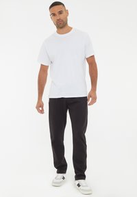 Weißes Kurzarm-T-Shirt, kombiniert mit schwarzen Jogginghosen und weißen Turnschuhen mit schwarzen Akzenten. Einfaches, lässiges Design.