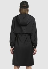 Černá proti dešti odolná bunda s kapucí, staženým pasem a elastickými manžetami. Má zkrácený design a voděodolný materiál.