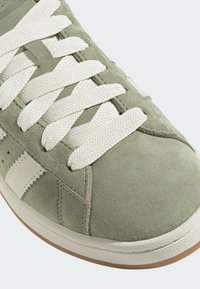 Zelené semišové tenisky s bielymi textúrovanými šnúrkami a krémovými koženými akcentmi. Obsahujú gumovú podrážku a diagonálne pruhy.