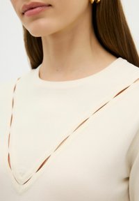 Beige Pullover mit V-Ausschnitt und Cut-out-Details sowie gerippten Texturen. Glatte Stoffqualität mit tailliertem Schnitt.