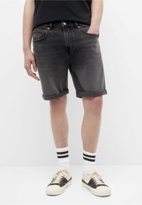 Shorts de mezclilla negros con dobladillo enrollado, cinco bolsillos y accesorios de cobre. Combinados con calcetines blancos de canalé con rayas negras y zapatillas.