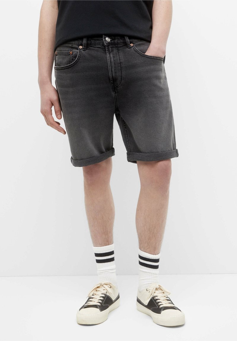 Shorts de mezclilla negros con dobladillo enrollado, cinco bolsillos y accesorios de cobre. Combinados con calcetines blancos de canalé con rayas negras y zapatillas.