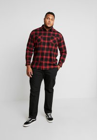 Rot-schwarzes Karomuster Flanellhemd mit langen Ärmeln und zwei Brusttaschen, kombiniert mit schwarzen Cargo-Hosen und schwarzen Turnschuhen.