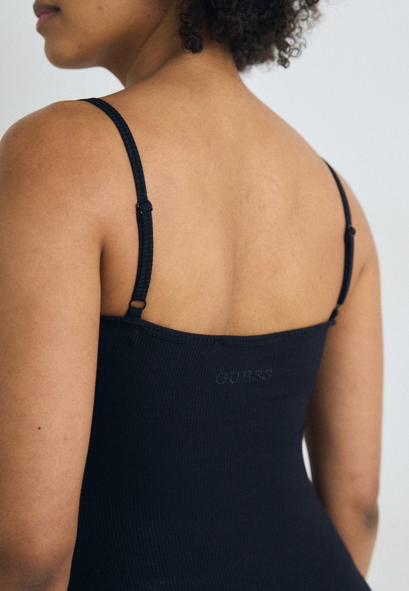 Débardeur noir à côtes avec des bretelles fines, comportant un détail de logo à l'arrière. Texture lisse et coupe ajustée.
