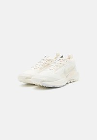 Zapatillas deportivas blancas con parte superior de malla texturizada, cordones planos y área del dedo del pie reforzada; presenta un diseño de suela ligeramente translúcida.