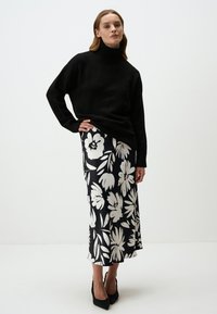 Zwarte gebreide coltrui gecombineerd met een zwart-witte satijnen rok met bloemen, featuring grote witte bloemen en een vloeiende silhouet. Zwarte hakken.