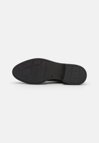 Suela de zapato negra con patrones texturizados, que cuenta con un tacón plano y la marca "Steve Madden". Material suave con bordes reforzados.
