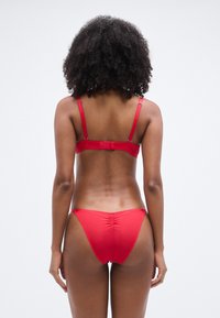 Κόκκινο μπικίνι δύο τεμαχίων με ρυθμιζόμενους ιμάντες και κούμπωμα, με άνετη ραφή και σούρες στην πλάτη.