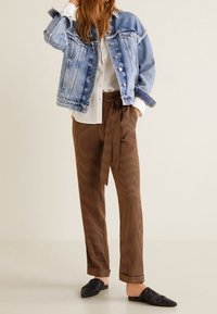 Giubbotto di jeans azzurro chiaro, camicia bianca sotto, pantaloni a righe marroni con cintura in vita e mules nere con texture.