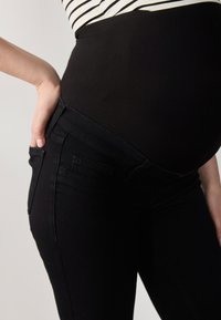 Svarta gravidjeans med en stretchig panel över magen, som har en smal passform och fickor. Tyget är mjukt och slätt, vilket ger komfort.