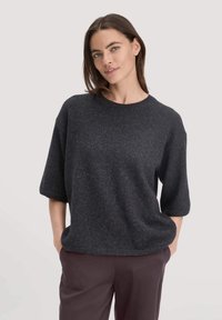 Maglione grigio scuro in maglia con scollo rotondo, maniche corte e vestibilità rilassata. Il tessuto sembra morbido con una leggera texture.