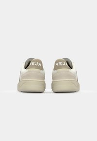 Hvite skinn-sneakers med beige suedeforsterkning og bakre strop; har subtil tekstur og merkevarelogo på hælen. Lavprofil design.