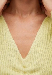 Pull jaune clair côtelé avec un col en V profond. Texture douce, coupe ajustée et détails minimalistes, mettant en valeur l'encolure.