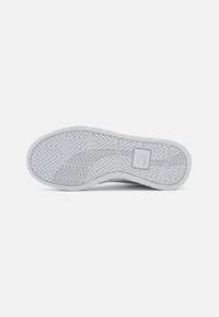 Hvid sneaker sål med et struktureret mønster, der har riller og et logo i midten. Fremstillet af gummi for greb og holdbarhed.