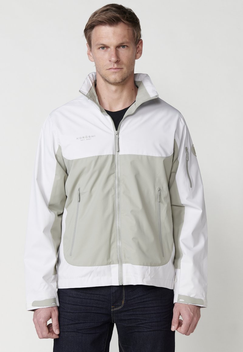 Veste légère et imperméable en gris et blanc, dotée d'un col haut, d'une fermeture éclair sur le devant, de poches latérales et de poignets réglables.