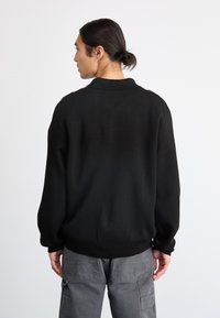 Maglione nero a maglia con colletto, polsini e orlo a coste. Texture liscia e vestibilità rilassata, mostrato da dietro.