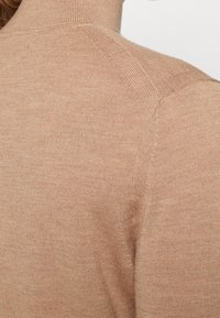 Beżowy sweter z dzianiny z golfem, o prążkowanej fakturze, dopasowanym kroju i detalach w szwie ramion. Miękka, lekka tkanina.